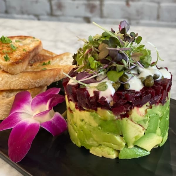 Vegan avocado and beet tartare with microgreens, capers, and toast points, garnished with an orchid.