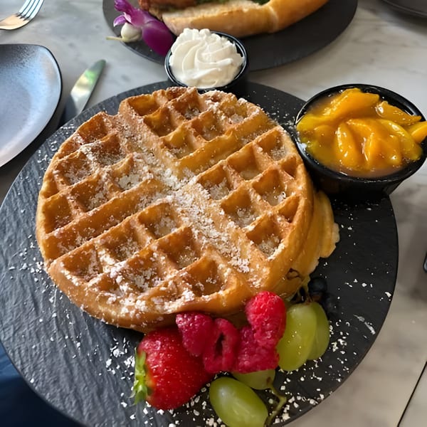 A vegan waffle with powdered sugar, fresh berries, grapes, mango compote, and whipped cream.