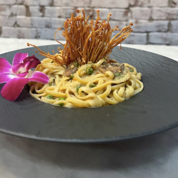 Vegan fettuccine pasta with creamy sauce, mushrooms, green onions, and crispy enoki, garnished with an orchid.