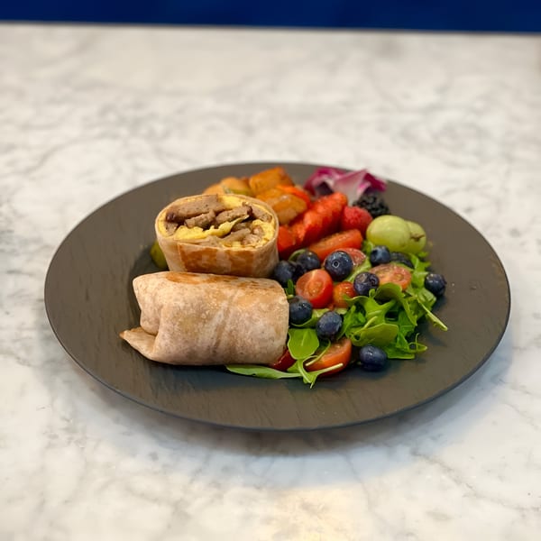 Vegan breakfast burrito with plant-based sausage and egg, served with fruit and a side salad.