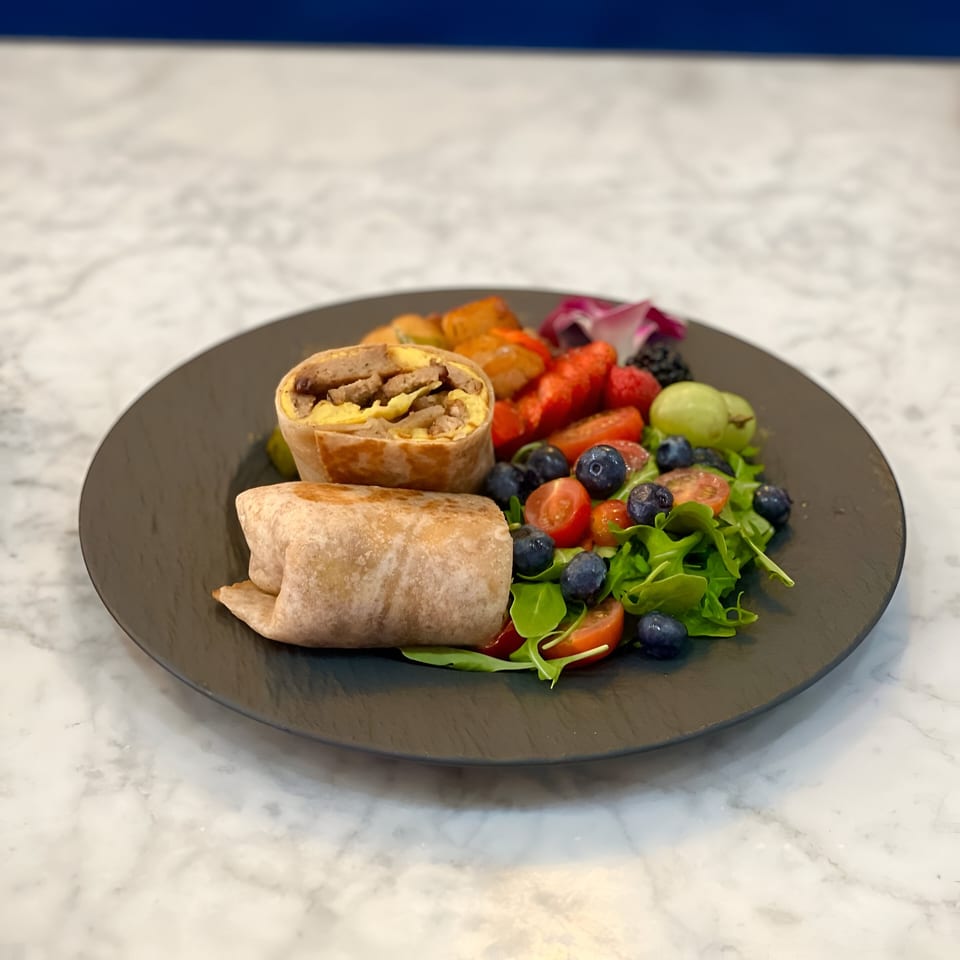 Vegan breakfast burrito with plant-based sausage and egg, served with fruit and a side salad.