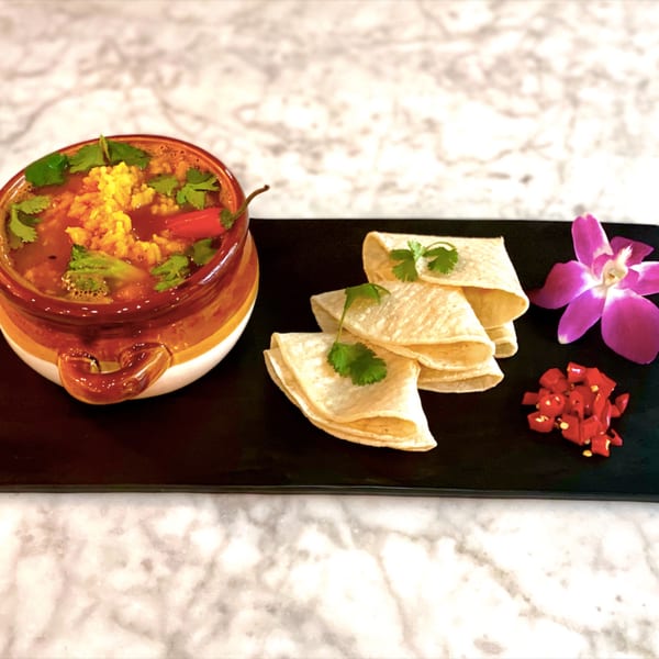 Vegan soup with rice, cilantro, and chili, served with tortillas and chopped chilies on a black tray.