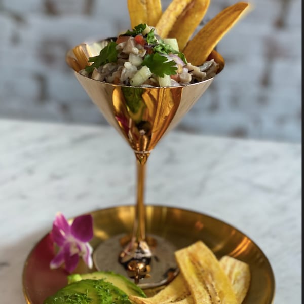Vegan ceviche in a golden martini glass, garnished with plantain chips, avocado, and an orchid.